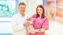 Prof. Dr. Clemens Tempfer, Direktor der Klinik für Frauenheilkunde und Geburtshilfe (l.) und Hebamme Vanessa Riese, die die Geburt begleitet hat, (r.) begrüßen Eleyna Sophie.