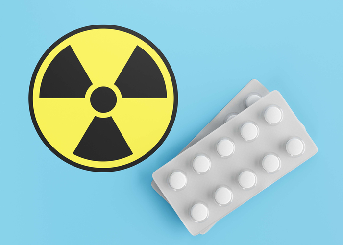 Medikamentenblister neben einem Radioaktivitätssymbol auf blauem Grund als Symbolbild für die Radiojodtherapie zur Behandlung einer Schilddrüsenüberfunktion